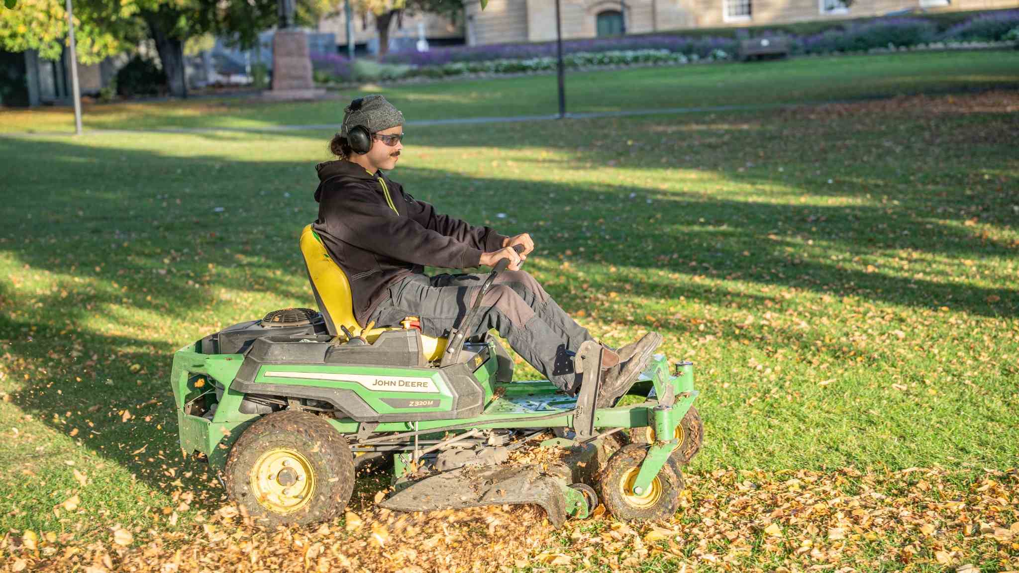 Aidan using a ride-on lawn mower to mow the grass and clear the fallen leaves